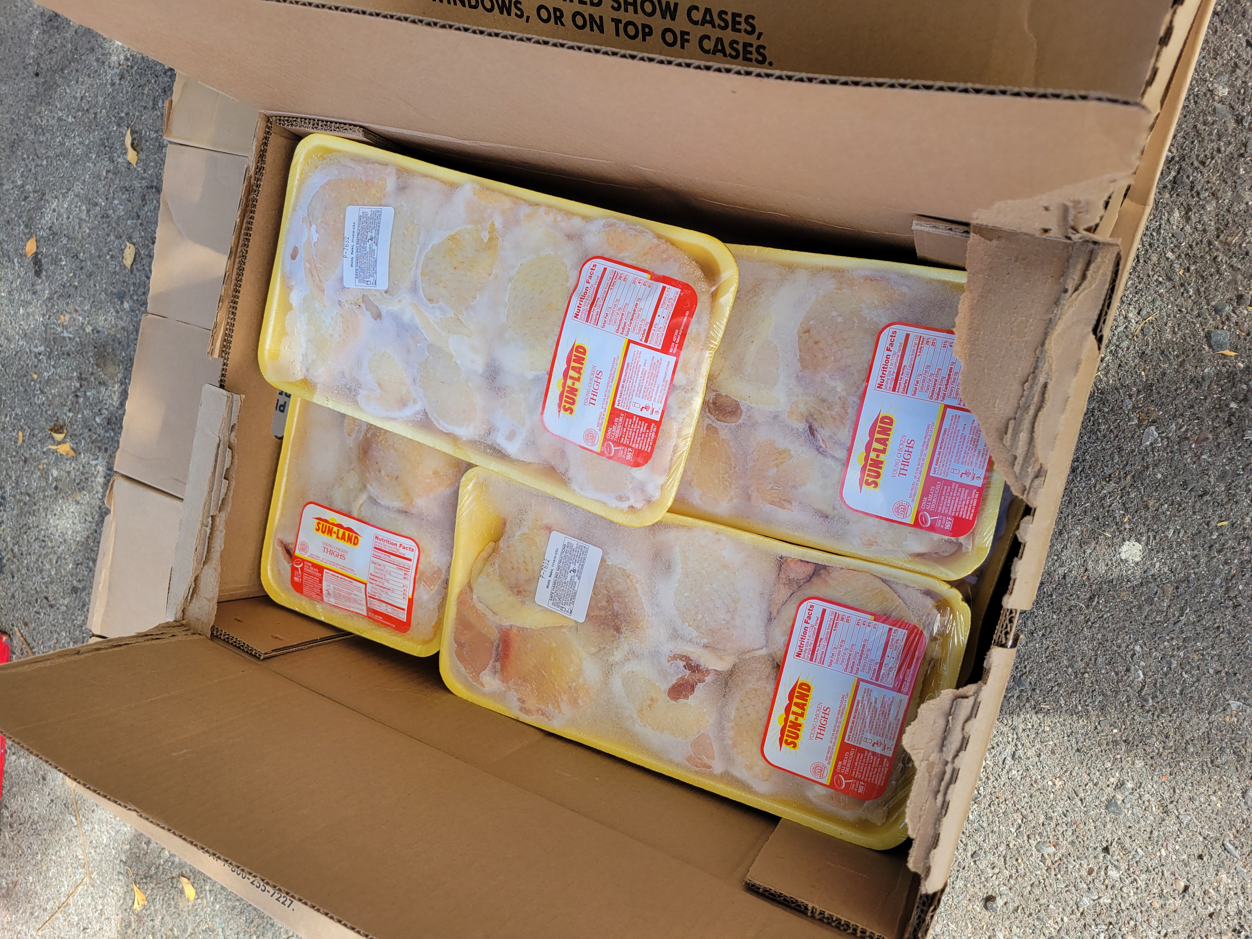 Cardboard box filled with containers of chicken thighs.